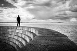 Man walking on a curved wall by the sea.