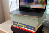 computer atop boxes and books on a dresser