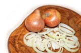 A wooden cutting board with layers of sliced onions.