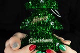 A woman’s hands with red, green and silver nail polish holding a small artificial green Christmas tree