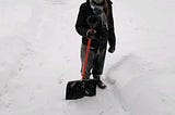 A woman with a snow shovel standing on a snowy sidewalk in Chicago
