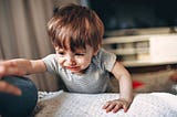 A toddler is crying and reaching for something on a couch
