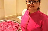 Woman in pink kurta wearing glasses, standing next to rose petals
