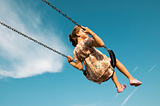 Young girl on a swing, with the background completely blue sky and clouds.