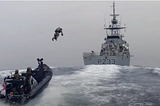 A Royal Marine in a jet pack launches from a fast boat to board a Royal Navy ship. Agile in action.