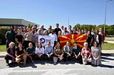 A group of Peace Corp volunteers posing at the Skopje Airport with the Peace Corps Fflag and the North Macedonia flag.
