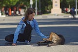 A girl sitting in a city square, playing with a dog