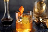 Old Fashioned Cocktail in a Modern Glass with a Large Ice Cube and Orange Twist