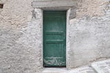 A faded green door in the middle of a stone wall