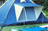 A tent surrounded by trees with a sleeping bag, cooler and camping chair