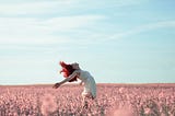 Woman in summer dress dances freely on a pink petaled flower field