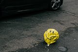 A deflated yellow balloon near a passing car laying on the street