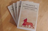 A number of paperback copies of the satirical SFF novel The League of Eponymous Jellyfish, by Matthew Clapham, sit on a desk, awaiting distribution to an eager global readership!