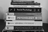 A black-and-white photo of a stack of psychology books, including titles on child psychology, social psychology, abnormal psychology, and general psychology.