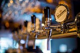 Six beer taps receding in focus towards a blurry window to daylight