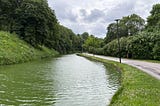 The photo shows a long pond with a walking and cycling path next to it.