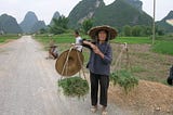 Three farmers on the road in Southern China’s Guangxi province. One is balancing two baskets filled with vegetables on pole. Fang-shaped karst-limestone hills in the background are found primarily in Southern China and Northern Vietnam.