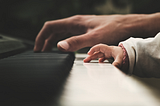 An adult hand and a baby hand touching a piano