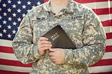 Army man before a U.S. flag holding a Bible