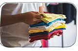 A person holding T-shirts that are folded in a store.