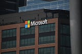 Microsoft headquarters building with colorful logo sign on dark metal facade under blue sky.
