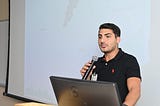 Close-up of Nazih with a microphone in front of a presentation screen.