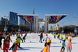 Young ice skaters skating with the Peace Gate behind them.