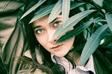 A woman looks out from behind green leaves.