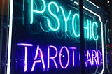 A neon sign in a shop window blares the words “PSYCHIC TAROT CARDS”