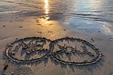 The words “Me” and “You” with circles around them, written in sand on the beach.
