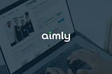 Photo of a person on a laptop checking fundraising progress on goaimly.com behind a faded dark blue background with the aimly logo front and center.