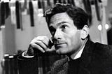 Em primeiro plano, Pier Paolo Pasolini olha para cima. Em segundo plano, vários negativos de fotos estão pendurados e secando em varais.