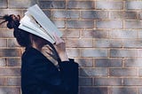 School Girl with Book in front of natural rustic red brick background holding book up to her face.