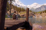 Protagonista de Life is Strange: True Colors sentada em um pier observando a paisagem de um lago, bosque e montanha