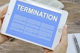 Hands of a person holding a white iPad with a blue screen with white font that reads “TERMINATION” with three columns of illegible text below.
