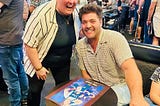 Wren Shealy (left) and CT Tamburello (right) share a fun moment at The Challenge Mania Live show in Zanies Rosemont. Wren is beaming while CT sits beside a signed Challenge poster, both caught mid-laugh during their unforgettable conversation about soup.