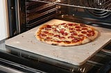 A pizza baking on a pizza stone in a home oven.