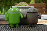 a green clay model of android bot and a earthen colored clay model of another android bot are standing next to each other on a table.