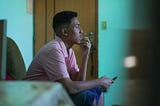 Young man sitting with hand on chin, smartphone in other hand