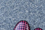 The toes of two buffalo plaid rainboots peak into a frame of distressed grey concrete.