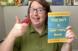 Myself holding up my latest book “This Isn’t a Self-Help Book” with a thumbs up and smiling.