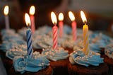 Cupcakes with blue swirled frosting and colourful lit birthday candles