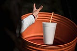 A woman throwing a soda into a trash can