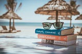 a photo of three books and sunglasses with the sea on the background