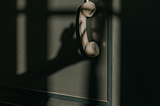 phone receiver hanging near a wall with the shadow of a hand behind it