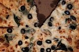 A close up of a pizza with black olives, spinach, and onion. There is one slice missing.