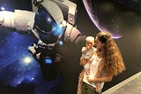 Mum holding a baby near astronaut picture in Finder office