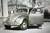 Black and white photo of a car with a woman standing by the open door
