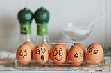 A carton of eggs with funny faces drawn on them in black marker.
