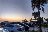 author’s white honda civic backed into a parking spot in the sand in a parking lot on Florida’s Gulf Coast, with palm trees and the sunset in the background